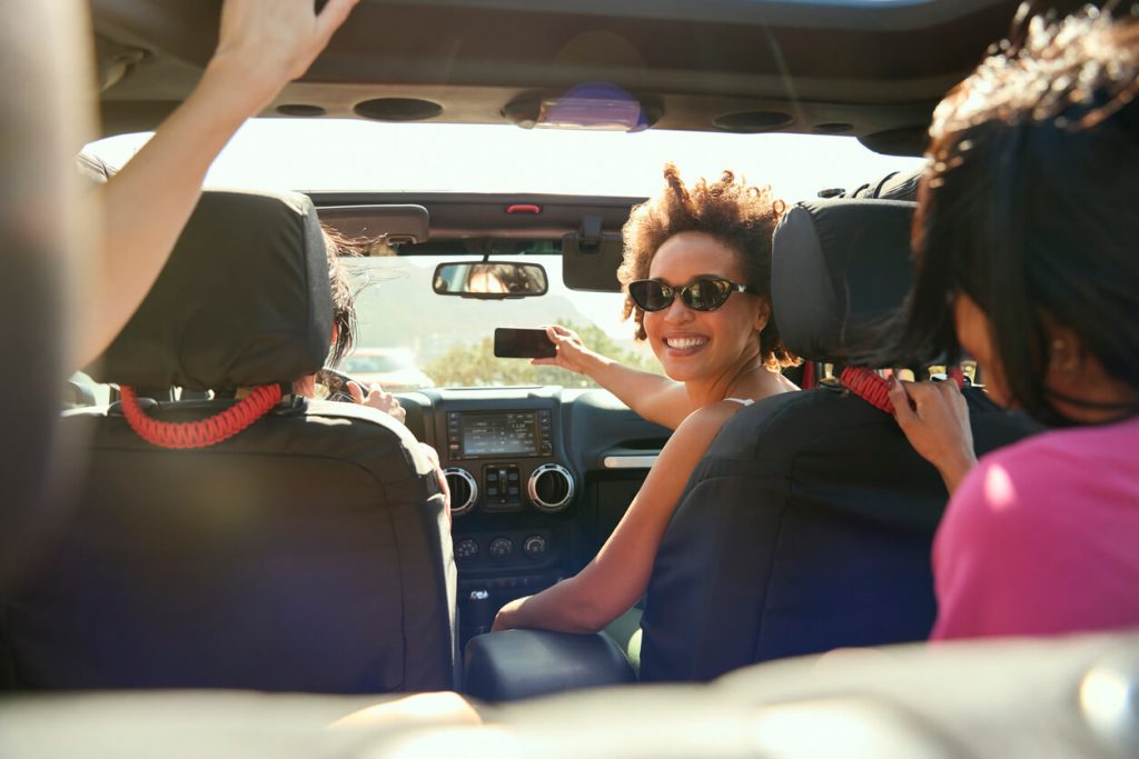 Laughing Female Friends Having Fun Posing For Selfie In Open Top Car On Road