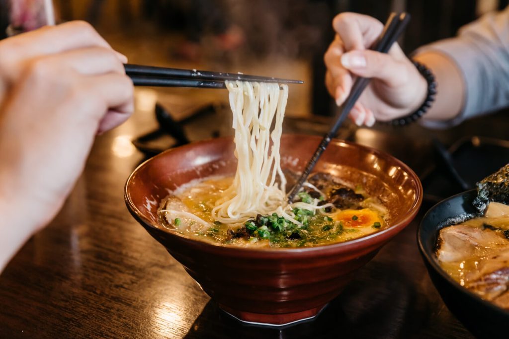 Best Time to Visit Japan: Man and woman hands pinching noodle in Ramen Pork Bone Soup 