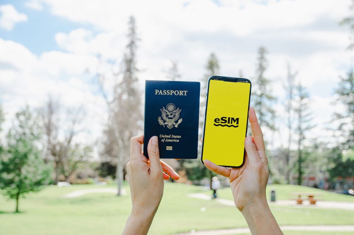 woman's hand holding up a U.S. passport and a smartphone with an eSIM background