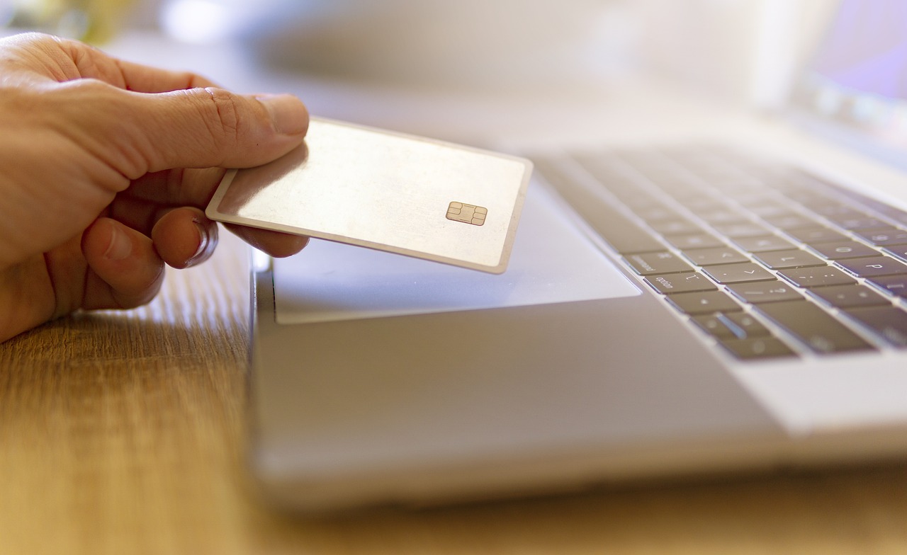 Man’s hand holding a credit card over an open laptop, representing online payment or digital purchase.