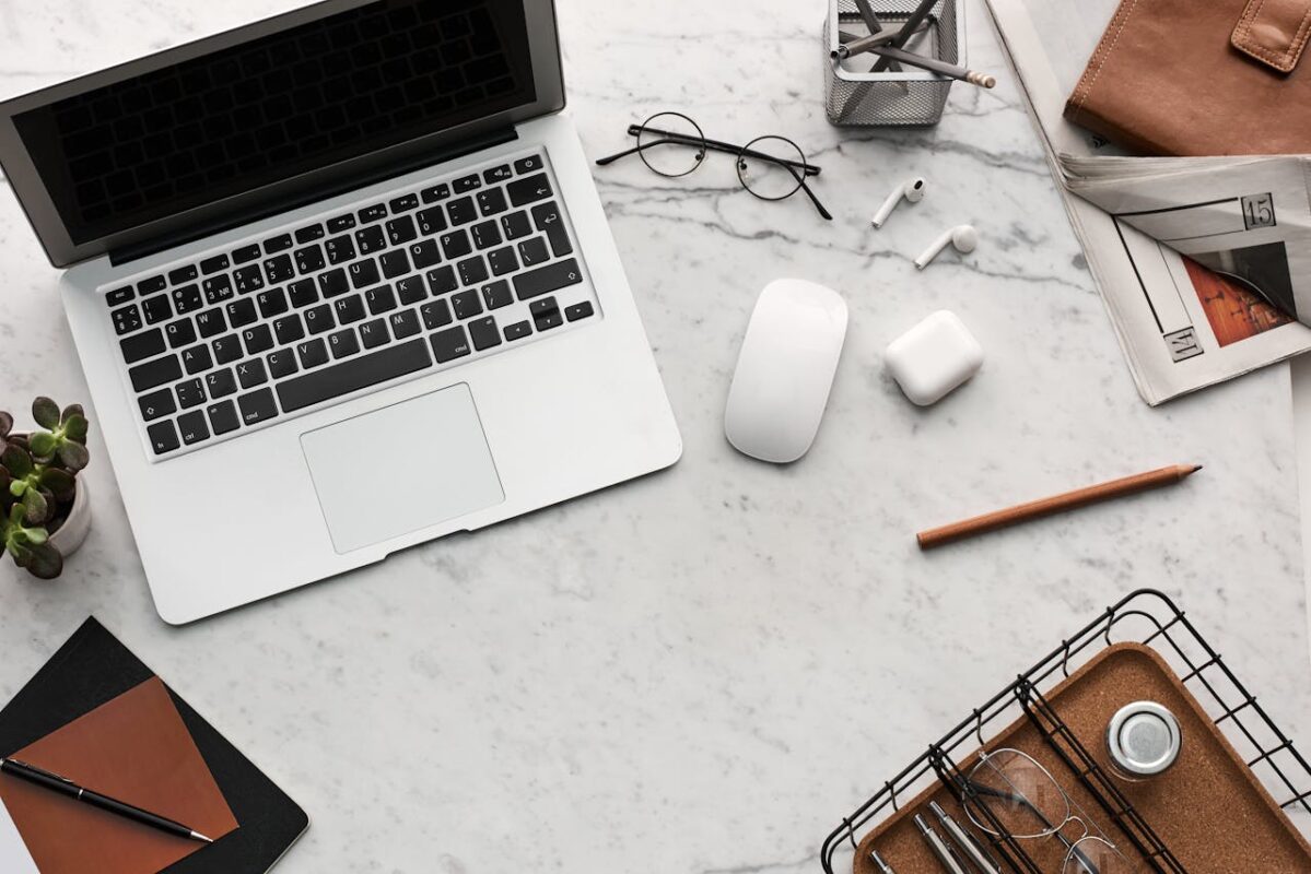Essentials for living abroad as an expat. Display of Electronics; MacBook, wireless mouse, EarPods and other gadgets next to Eyeglasses.