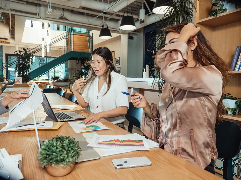 Two women working in an office with laptops and report notes, discussing projects related to the best countries for remote workers
