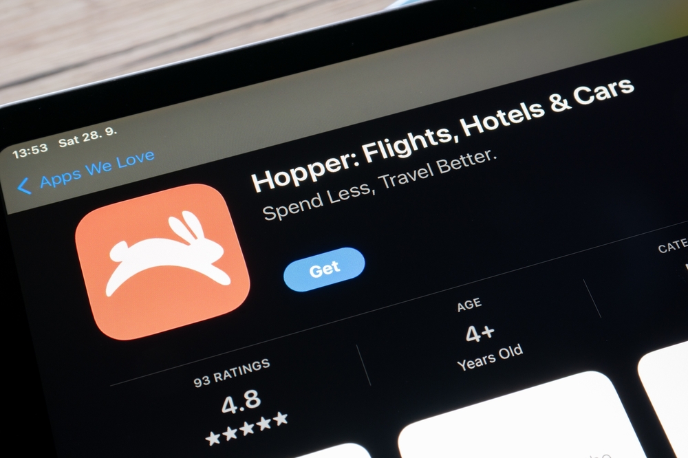 A close-up shot of a tablet screen displaying the App Store page for the Hopper app. The app's orange logo with a white rabbit is visible, along with the title 'Hopper: Flights, Hotels & Cars' and its tagline. The image represents the kind of effective Alert Services that can help travelers find great deals on flights.